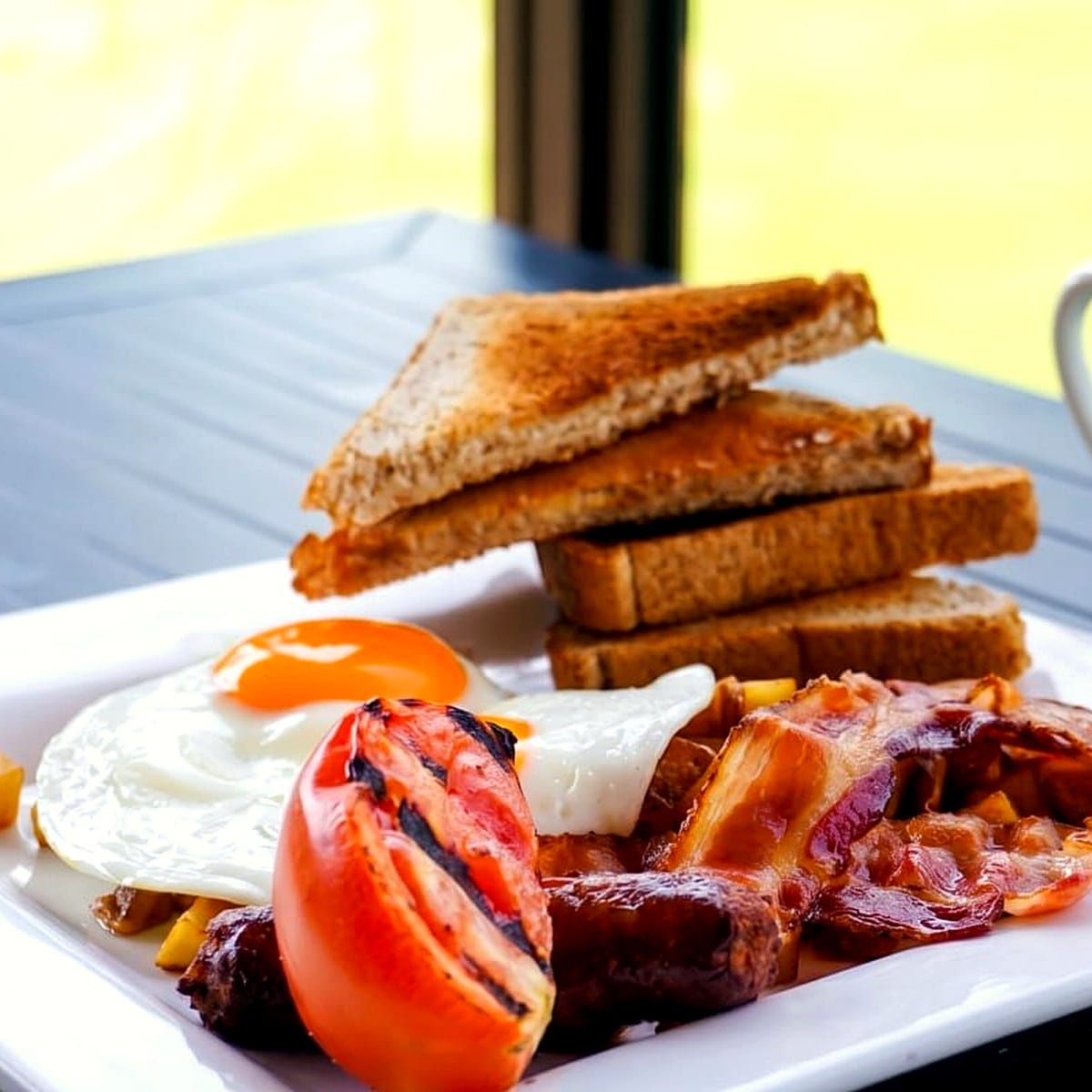 Two eggs, sausage, bacon, grilled tomato and toast on a Bistro plate