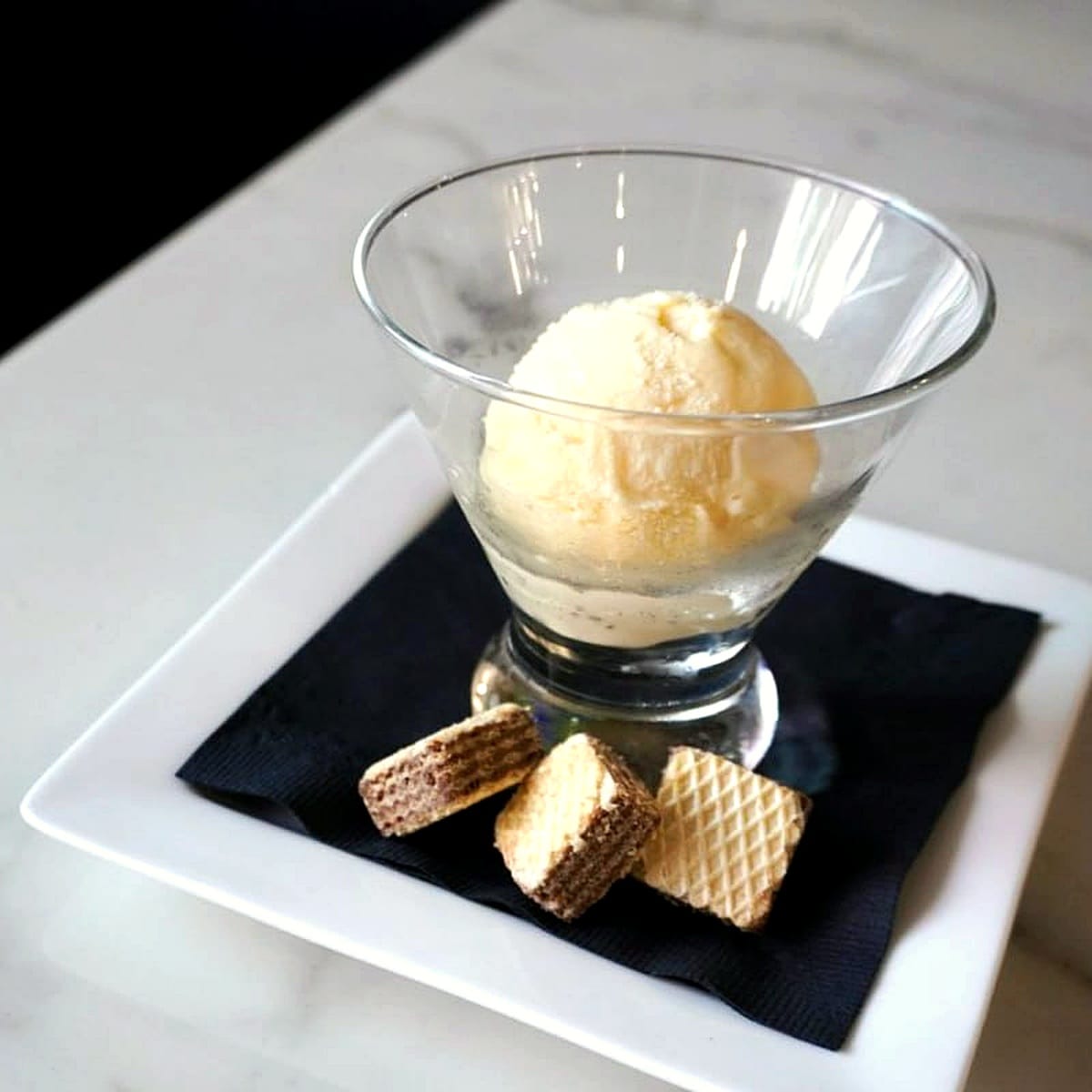 A scoop of vanilla ice cream with wafer cookies on a black napkin and marble counter