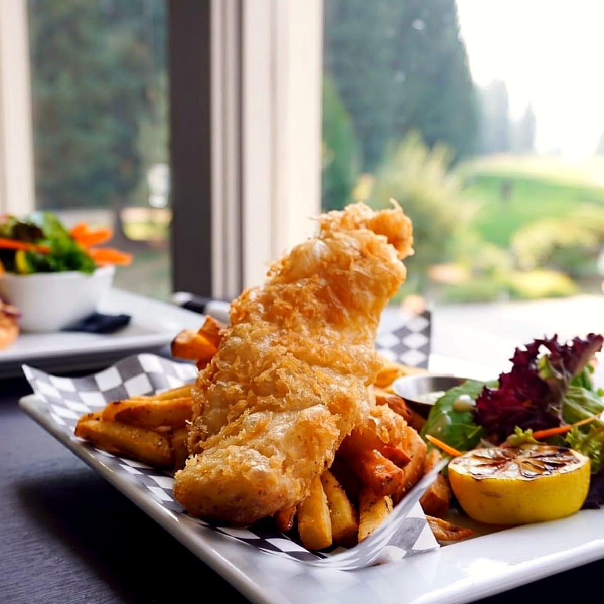 Beer-battered snapper and fries with a side salad and a grilled lemon, course window behind