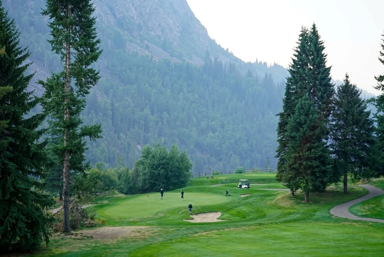 A foursome on the green at Birchbank with cart parked on the cart path, the Selkirks rising behind