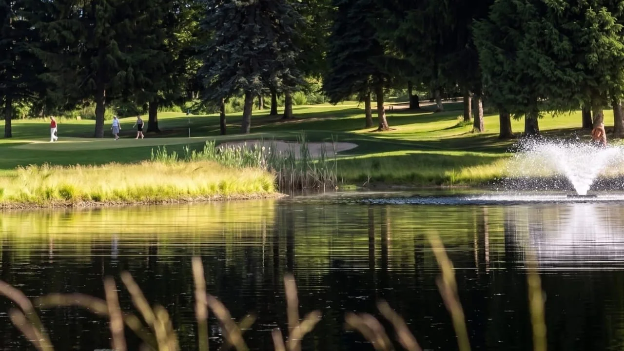 The pond and fountain at Birchbank with the fairway and trees beyond, distant players walking off the green